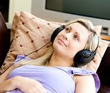 Happy woman listen to music wearing headphones lying on a sofa