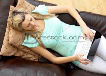 Cute woman using a laptop lying on a sofa