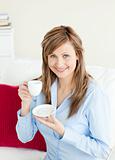 Glowing businesswoman holding a cup sitting on a sofa 