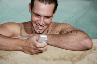 Male texting on mobile phone in swimming pool on holiday
