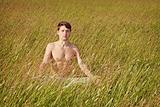 Man sits in grass in lotus pose