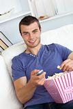 Charming young man eating popcorn watching television