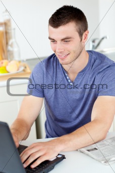 Positive young man using his laptop in the kitchen