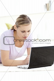 Concentrated woman using her computer lying on the floor 