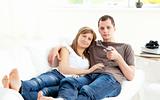 Positive caucasian couple watching tv lying on the sofa 