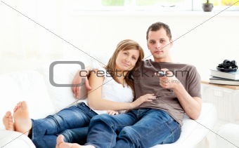 Positive caucasian couple watching tv lying on the sofa 