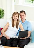 Enthusiastic couple using laptop smiling at the camera 
