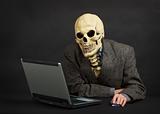 Terrible skeleton sits at black office with laptop