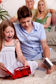 Kids opening christmas gifts with parents in the background