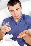 Dejected young man holding pills and water sitting on the sofa