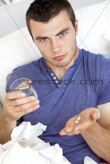 Dejected young man holding pills and water sitting on the sofa