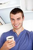 Charming caucasian man holding a cup of coffee smiling at the ca