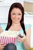 Bright caucasian woman holding a remote and popcorn