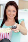 Jolly woman sitting on sofa with popcorn holding a remote