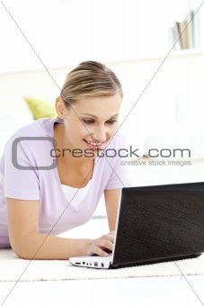 Radiant young woman using her laptop lying on the floor 