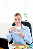 Cheerful young businesswoman drinking coffee smiling at the came