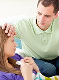 Assertive man feeling temperature of his ill girlfriend holding tissue lying on a sofa