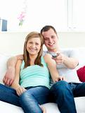 Glowing young couple sitting on the sofa watching tv 