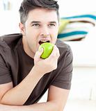 Young man lying on the ground and eating a green apple