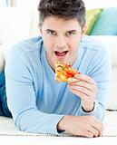 Young man lying on the ground and eating pizza 