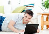 Positive young man using his laptop lying on the floor