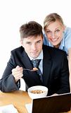 Enamored couple of businesspeople smiling at camera eating cerea