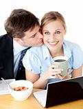 Young businessman kissing his delighted girlfriend having breakfast