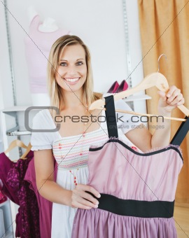 Bright caucasian woman holding a dress smiling at the camera 