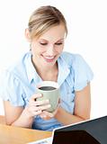 Smiling businesswoman drinking coffee using her laptop 