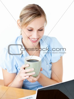 Smiling businesswoman drinking coffee using her laptop 
