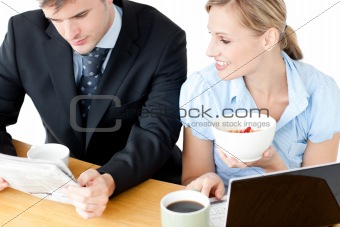 Happy couple of businesspeople having breakfast reading the news