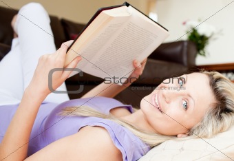 vCharming young woman reading a book lying on the floor 