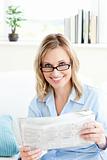 Charming businesswoman reading the newspaper sitting on the sofa at home