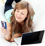 Lively caucasian woman lying on the sofa with laptop and card in the living room