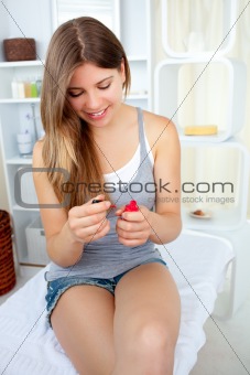 Glowing young woman varnishing her nails with red nail polish