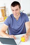Charming young man using his laptop holding orange juice 