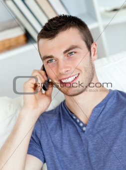 Charismatic young man talking on phone sitting on the sofa 