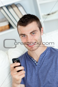 Charming young man sending a text smiling at the camera 