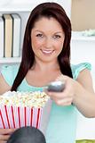 Cute caucasian woman holding a remote and popcorn looking at the
