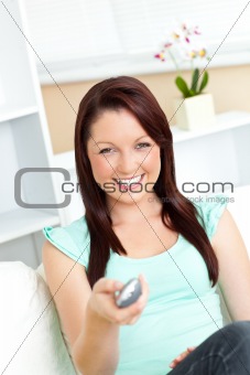 Joyful caucasian woman holding a remote smiling at the camera