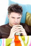 Ill depressed  man holding a cup of coffee lying on the sofa