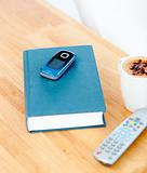 Close-up of a book,cellphone,remote and cup of coffee on the tab