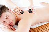 Positive young man enjoying a back massage with hot stone 