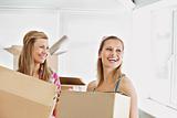 Laughing female friends holding boxes after moving 