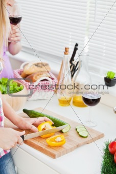 Close-up of two young woman cutting paprika and cucumber for a s