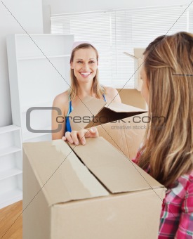 Two radiant female friends holding boxes after moving