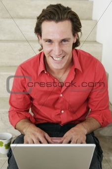 Young male working on laptop on stairs and looking to camera