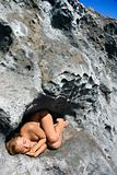 Nude woman sleeping on rock.