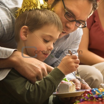 Father helping boy with cake.