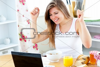 Enthusiastic young woman looking at her laptop with arms up 